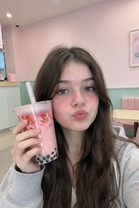 A teenage girl holding a strawberry boba tea next to her face