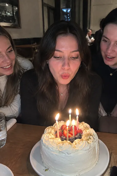 Young woman blowing out candles on a berry birthday cake beside her friends