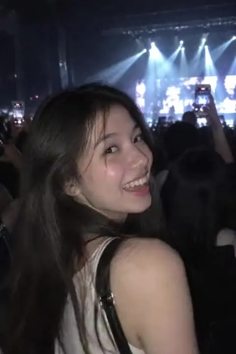 A young woman smiling over her shoulder at a concert, a still photo
