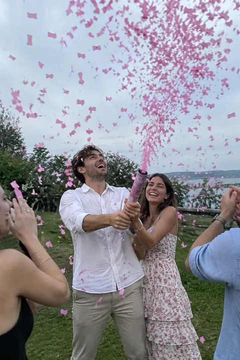 A couple celebrating outdoors as pink confetti falls around them surrounded by friends