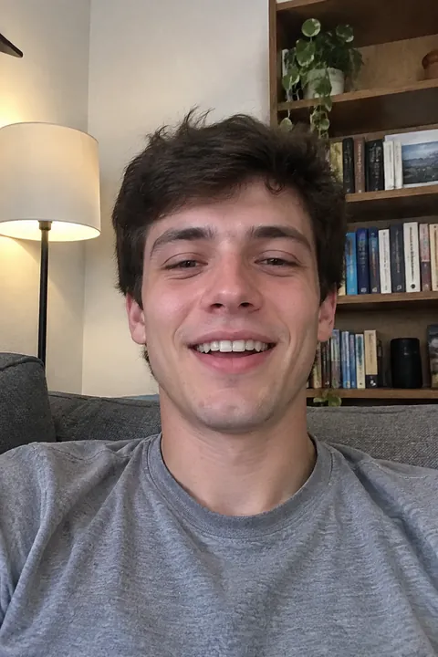 Young man laughing heartily while sitting on a sofa beside a bookshelf