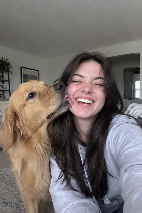 A young woman laughing while her golden retriever licks her cheek