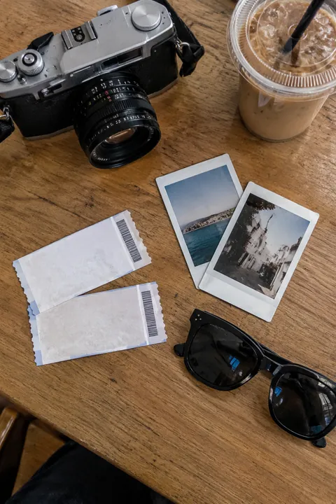 A table from above with a film camera, ticket stubs, polaroids, sunglasses and an iced coffee