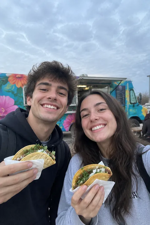 Two friends taking a selfie with tacos in front of a food truck
