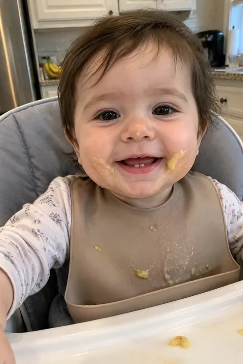 A messy baby sitting in a high chair smiling with eyes closed