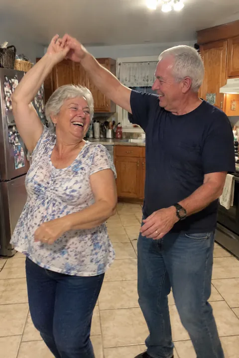 An older couple smiling and dancing together in a home kitchen