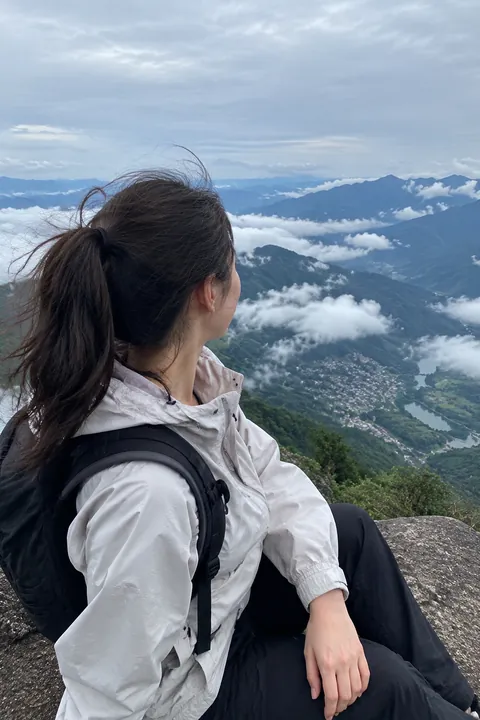 A woman sitting on a rock overlooking a cloudy mountain valley