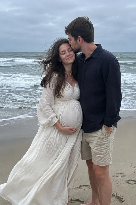 A pregnant woman and a man standing together lovingly on an overcast beach