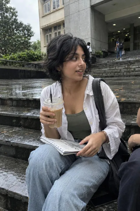 A young woman sitting on wet steps with an iced coffee and a sketchbook