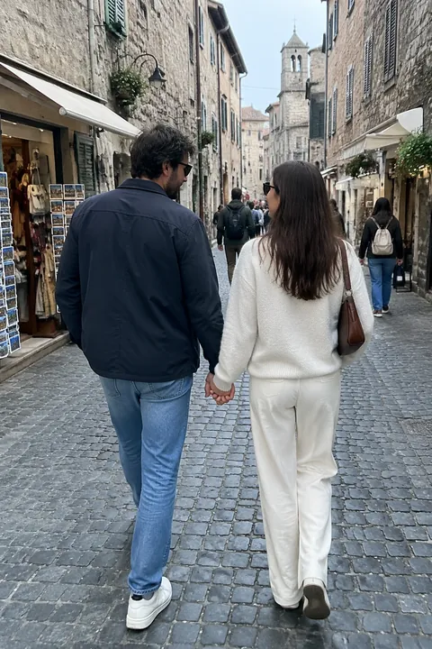 A couple holding hands walks down a narrow cobblestone street in an old town
