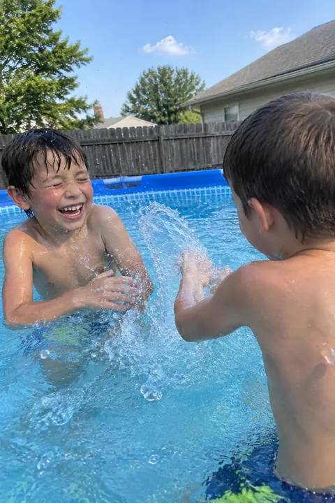 Two young boys smiling and splashing water in an above-ground backyard swimming pool