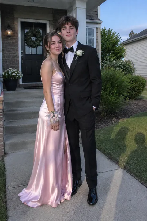 Young couple dressed in formal prom attire posing together outside a suburban house