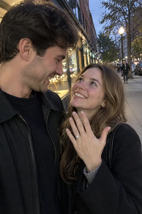 A newly engaged couple smiling together on a city sidewalk at dusk