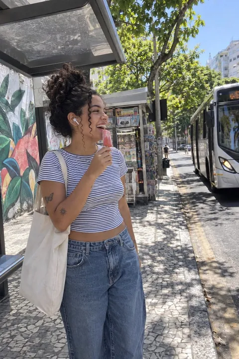 A woman with curly hair holding an ice pop at a bus stop, shot at normal zoom