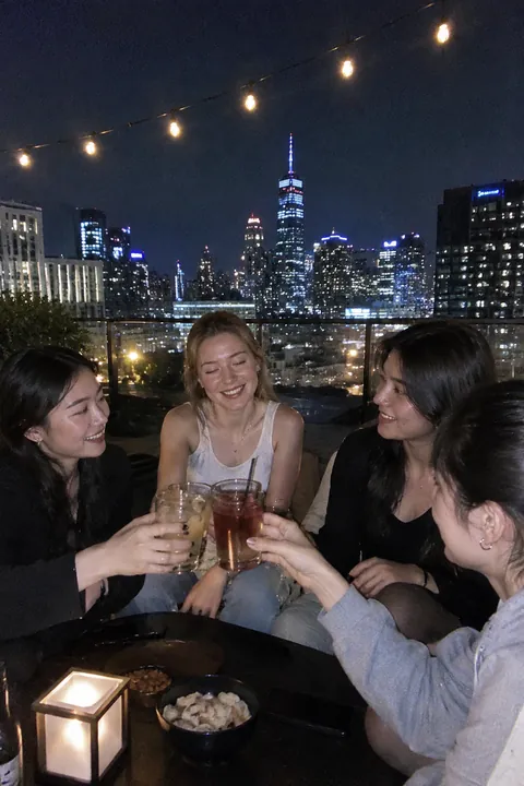 Four young women toasting with drinks at a rooftop bar at night