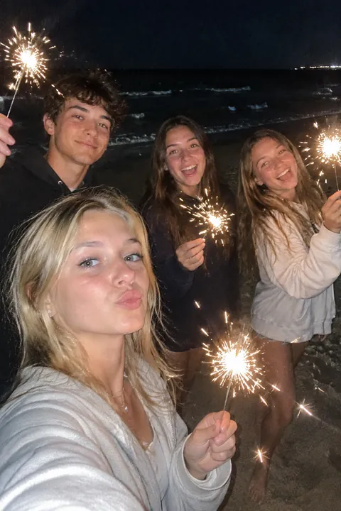 Four young friends holding lit sparklers on a beach at night
