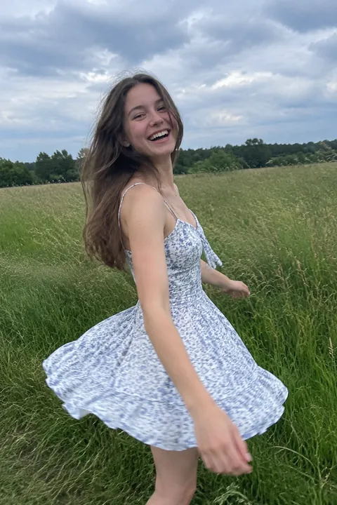Smiling young woman in a floral dress twirling in a grassy field