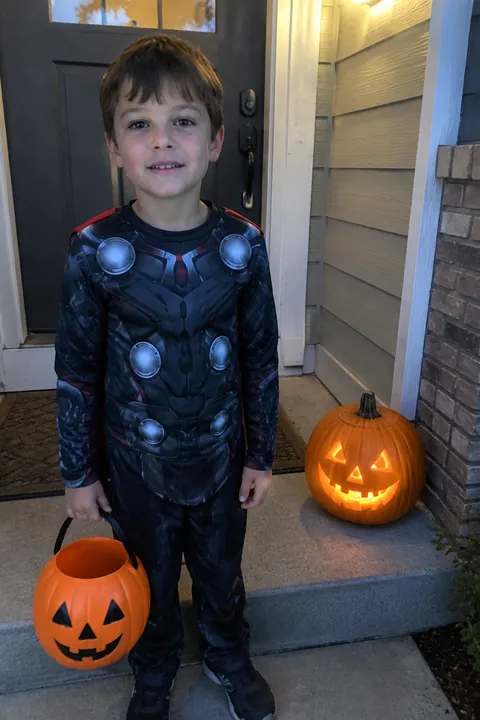 A boy with a candy bucket at a front door, a jack-o'-lantern on the step