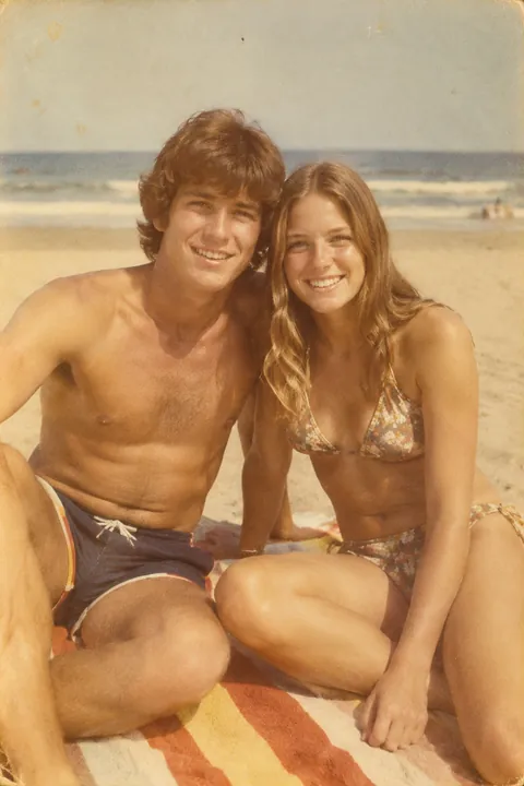 A young smiling couple sitting together on a striped beach towel